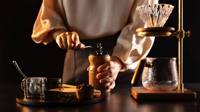 Handmatige koffiemolen op een tafel met koffiebonen en gemalen koffie ernaast.