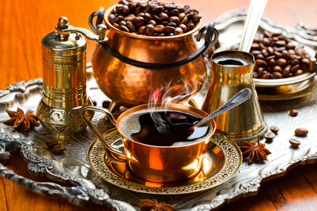 Een overzichtelijke afbeelding van een ibrik, koffiemolen, en de ingrediënten (koffiebonen, suiker, water) in één frame.