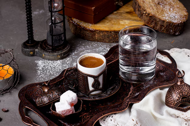 en afbeelding die laat zien hoe Turkse koffie traditioneel wordt geserveerd met een glas water en zoetigheid.