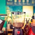 Close-up of coffee grinders and cups in a colorful cafe setting.